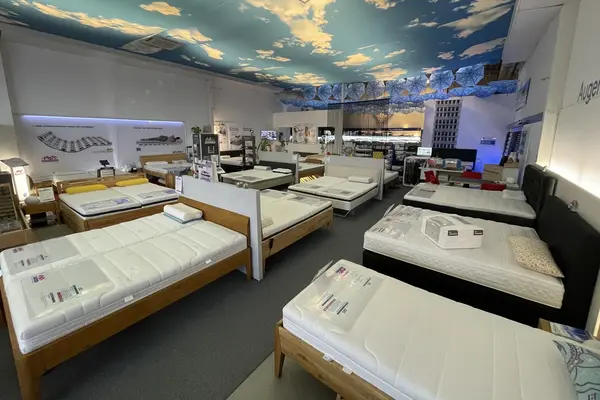 Matratzen und Betten in einem modernen Fachgeschäft mit beleuchtetem Himmelmotiv.